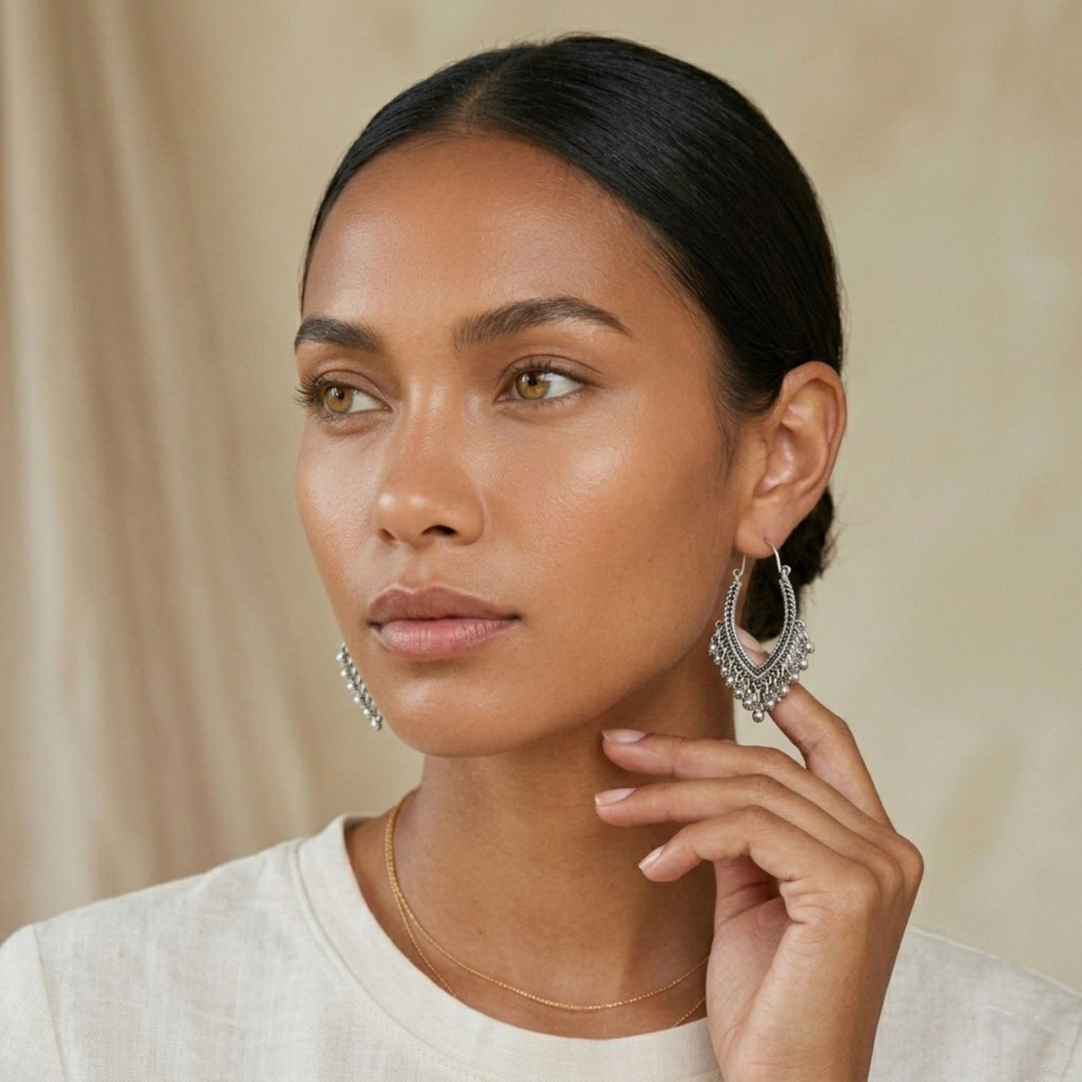 Woman wearing silver hoop earrings against a beige background. Priya_Vintage_Metal_Earrings_-_The_Songbird_Collection_