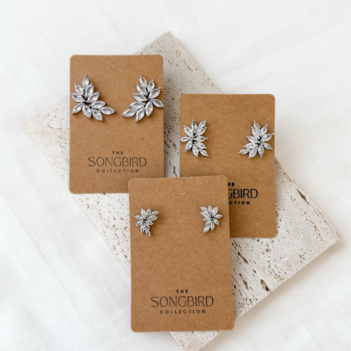 Three pairs of silver floral earrings on brown 'The Songbird Collection' cards.
