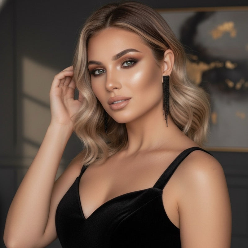 Woman in a black dress posing with one hand by her face against a dark background