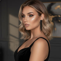 Woman with styled hair and black earrings wearing a black dress against a dark background