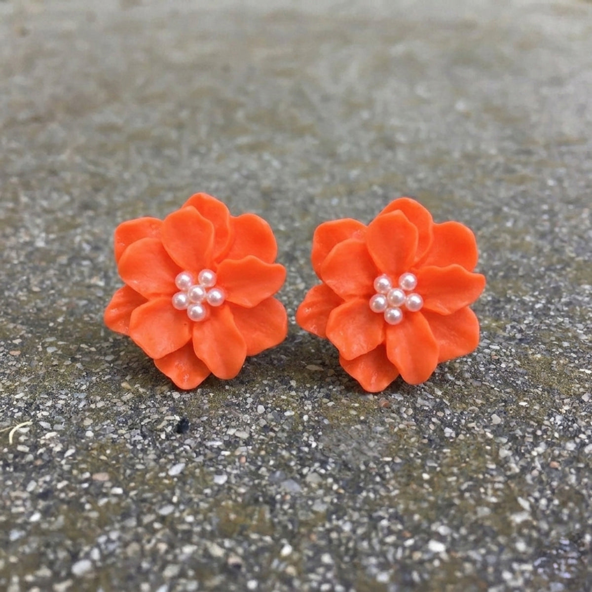 Pair of orange flower-shaped earrings with pearl centers on a gray surface. Rosalie Earrings - The Songbird Collection
