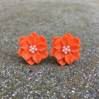 Pair of orange flower-shaped earrings with pearl centers on a gray surface. Rosalie Earrings - The Songbird Collection