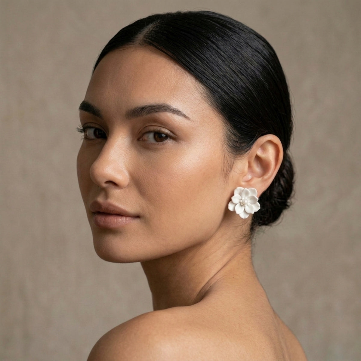 Woman wearing a white floral earring against a neutral background