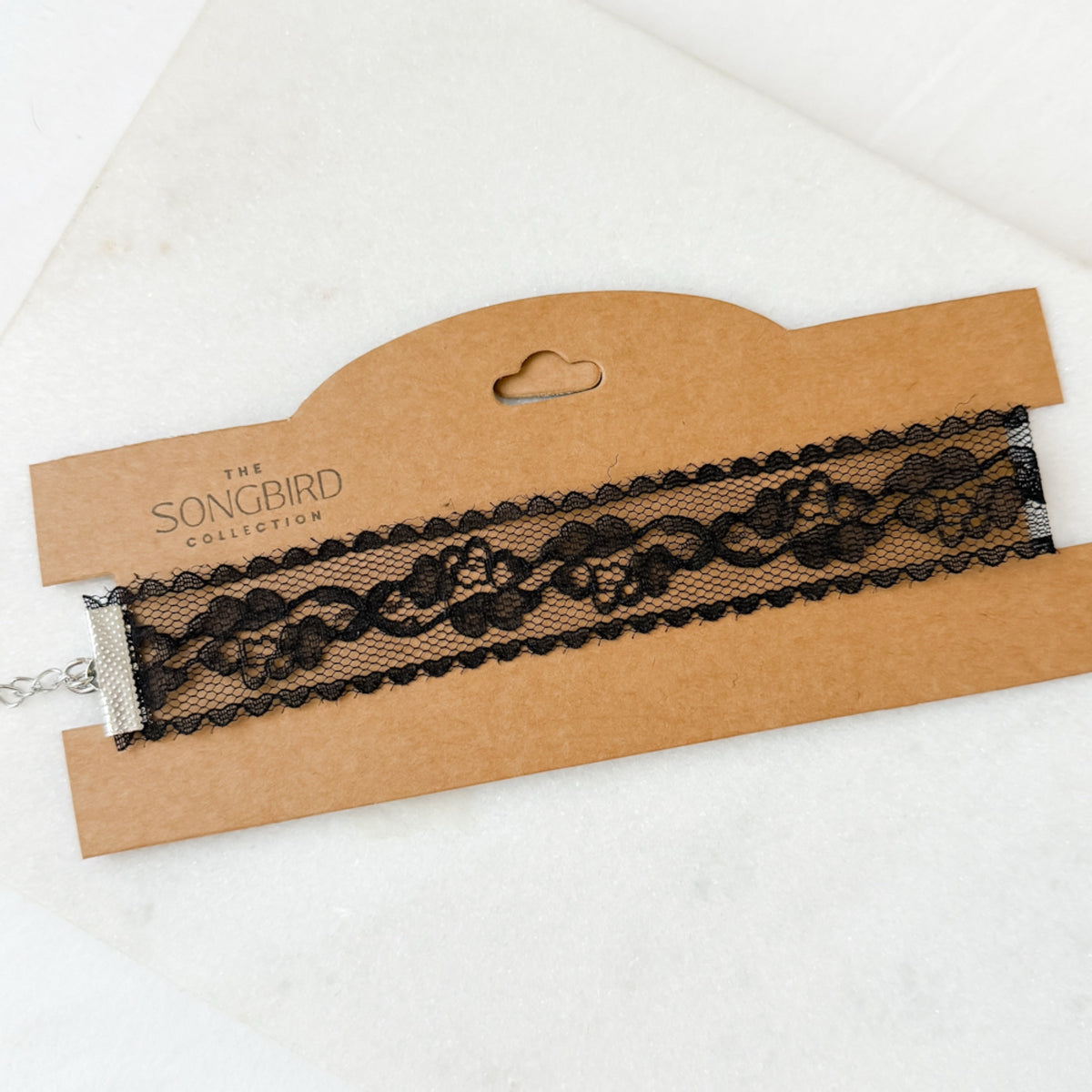 Black lace choker on a cardboard holder with 'The Songbird Collection' branding.