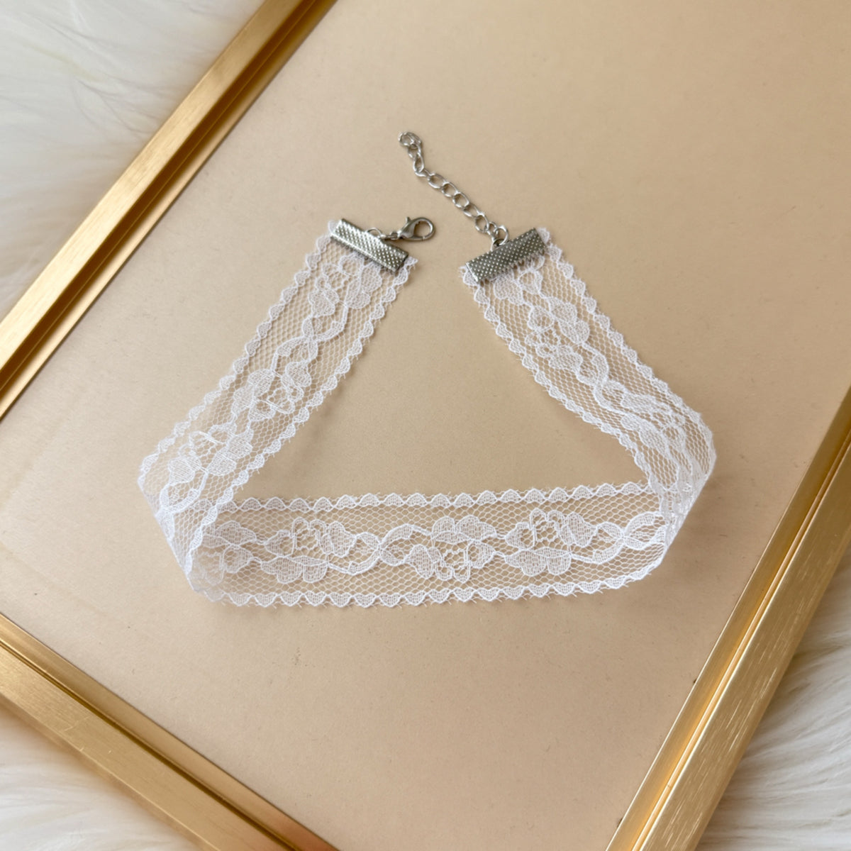White lace choker necklace on a beige background with a gold frame.