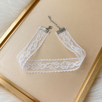 White lace choker necklace on a beige background with a gold frame.
