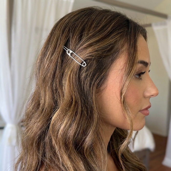 A woman in profile wearing a silver safety-pin style hair clip in her brown and blonde highlighted hair, set against a softly blurred indoor background with white curtains. Safety Pin Hair Pin Set - The Songbird Collection