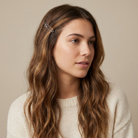 A woman with long, wavy brown hair wearing a small silver safety-pin hair clip on the side of her head, paired with a cream-colored knit sweater, set against a solid beige background.  Safety Pin Hair Pin Set - The Songbird Collection