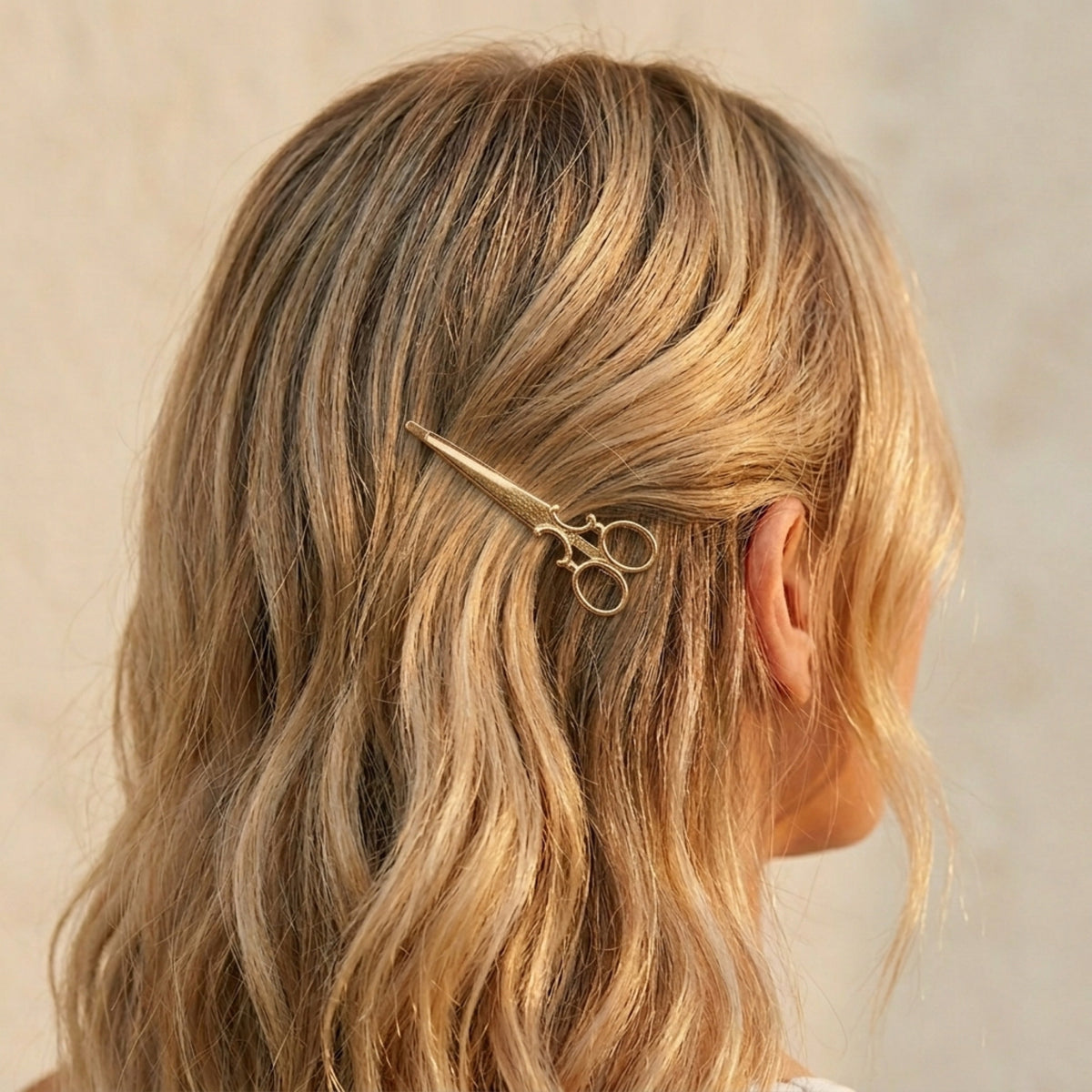 Person with wavy blonde hair wearing a gold scissors-shaped hair clip on a neutral background