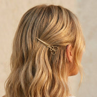 Person with wavy blonde hair wearing a gold scissors-shaped hair clip on a neutral background