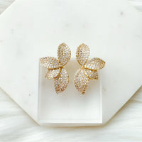 Gold leaf-shaped earrings on a white marble surface. Seraphine Earrings - The Songbird Collection - pave - floral petal