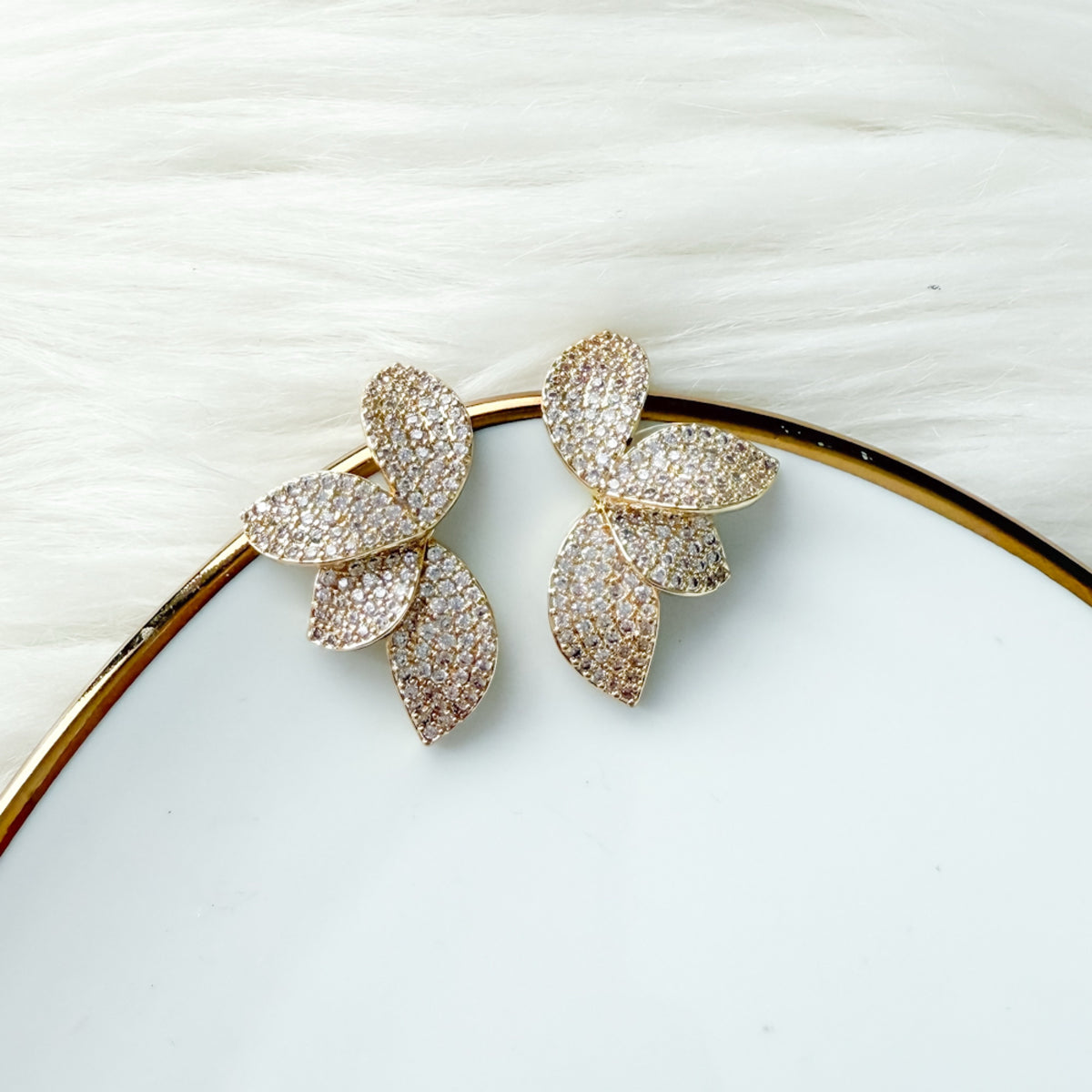 Gold leaf-shaped earrings on a white plate with a white background. Seraphine Earrings - The Songbird Collection - pave - floral petal