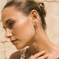 Close-up of a woman wearing gold leaf earrings with a neutral background