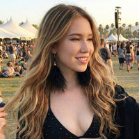 Woman in a black bikini top and feather earrings at a music festival with a crowd in the background