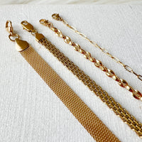 A collection of five stainless steel bracelets with gold plating, displayed in a row on a textured background.