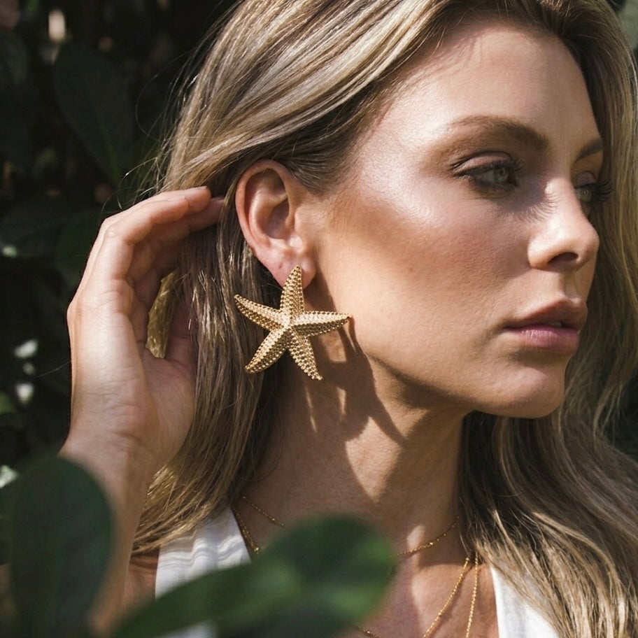 Woman wearing gold starfish earrings with a blurred natural background  Starfish_Statement_Earrings_-_The_Songbird_Collection_