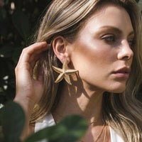Woman wearing gold starfish earrings with a blurred natural background  Starfish_Statement_Earrings_-_The_Songbird_Collection_