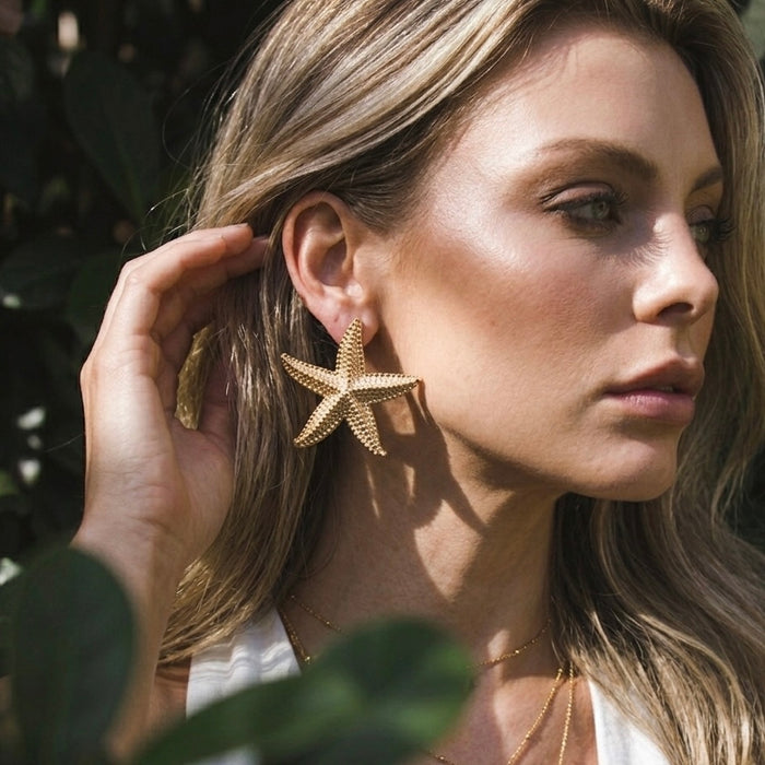 Woman wearing gold starfish earrings with a blurred natural background  Starfish_Statement_Earrings_-_The_Songbird_Collection_