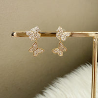 Butterfly-shaped earrings with gold frame on a neutral background