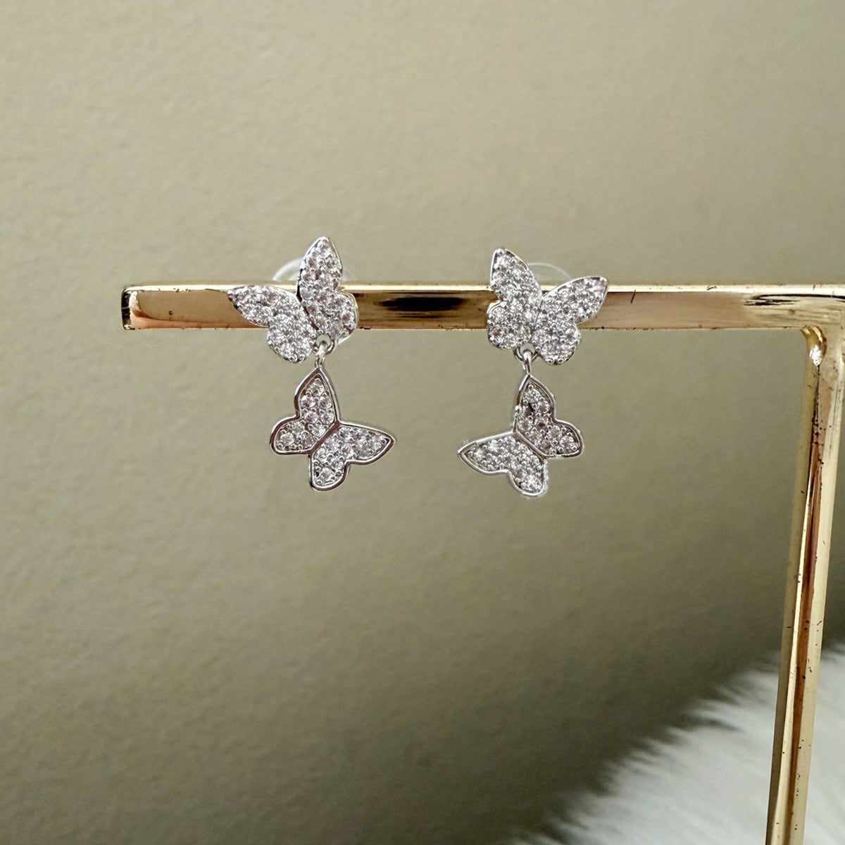 Butterfly-shaped earrings on a gold stand against a beige background