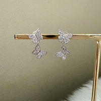 Butterfly-shaped earrings on a gold stand against a beige background