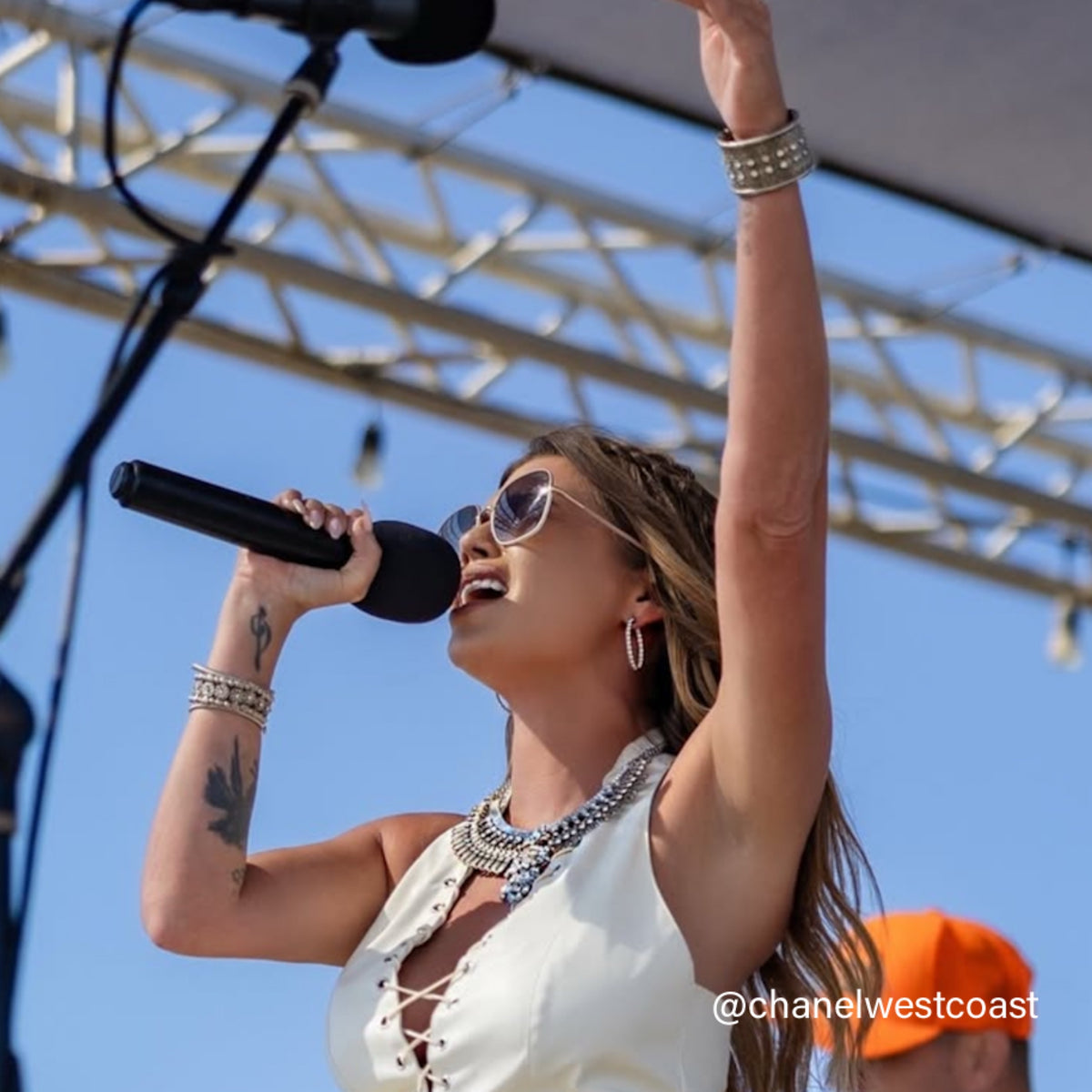 Chanel West Coast singing into a microphone with a clear blue sky in the background