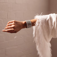 A person's forearm wearing a vintage metal bracelet with a silver tone and beaded design, protruding from a white furry sleeve.