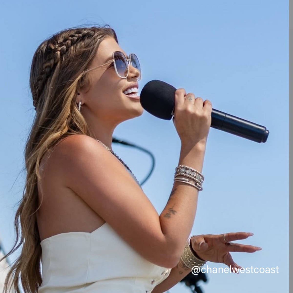 Woman singing into a microphone against a clear blue sky
