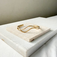 Gold bracelet  double wavy lines on a textured stone surface. The Contour Cuff Bracelet - The Songbird Collection