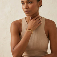 Woman wearing a beige ribbed tank top and gold bracelet against a neutral background