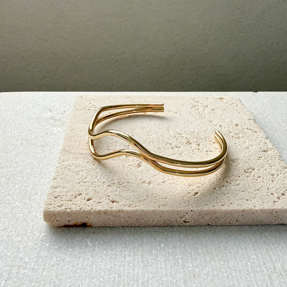 Gold bracelet  double wavy lines on a textured stone surface. The Contour Cuff Bracelet - The Songbird Collection
