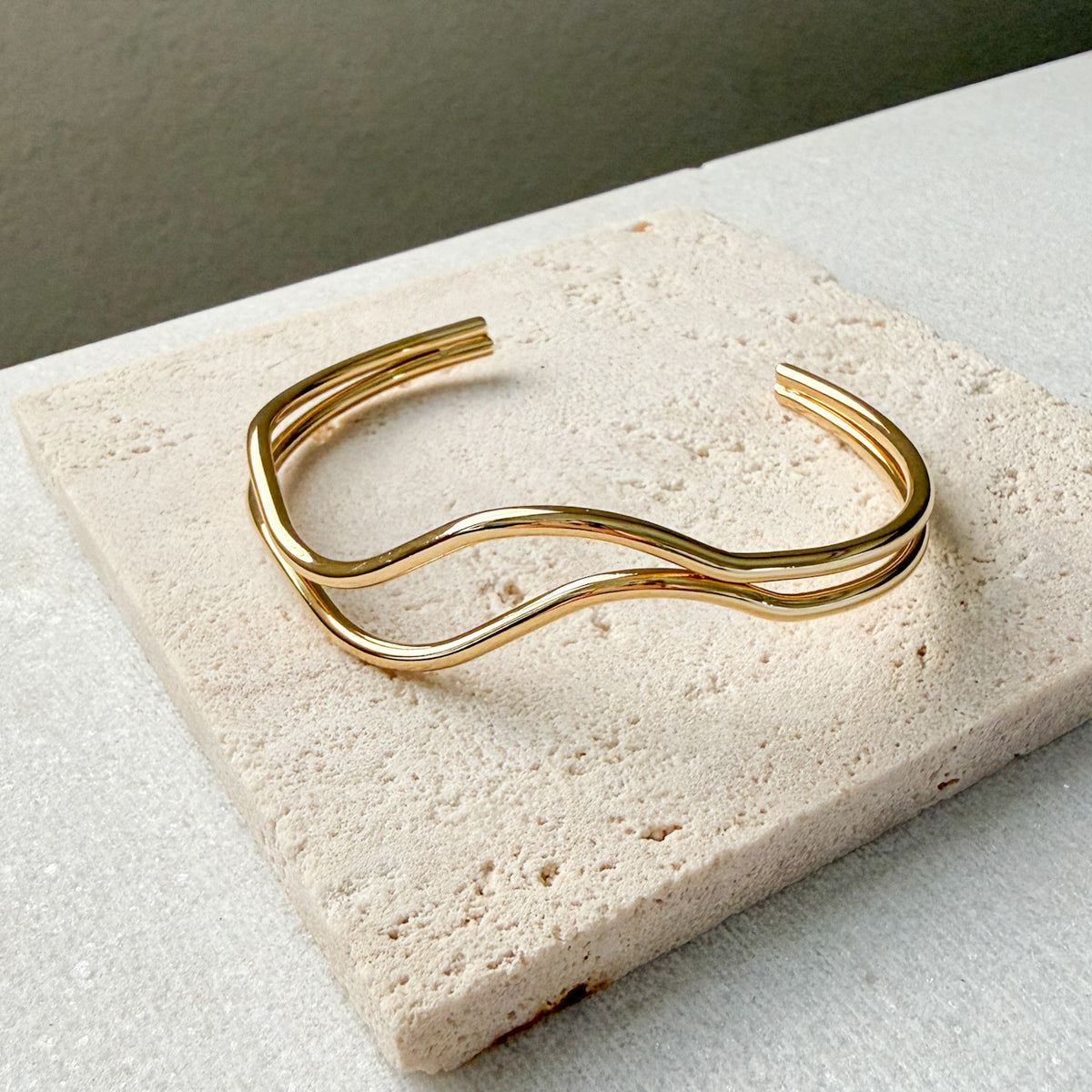 Gold bracelet  double wavy lines on a textured stone surface. The Contour Cuff Bracelet - The Songbird Collection