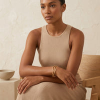 Woman wearing a beige sleeveless dress sitting in a minimalistic setting. - The Contour Cuff Bracelet - The Songbird Collection