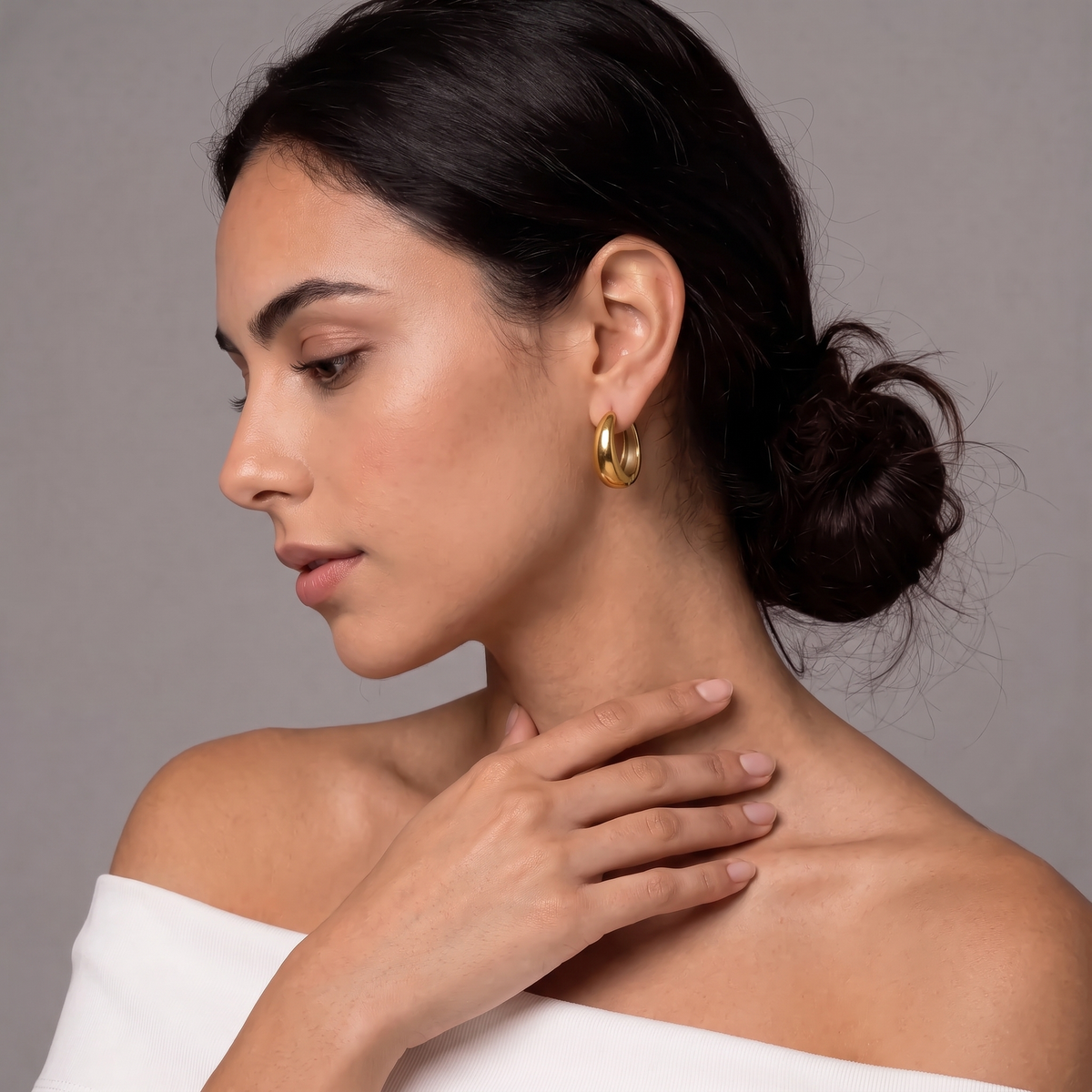 A woman in profile wearing a chunky, polished gold hoop earring, set against a neutral gray background.  The Ever Teardrop Hoop Earrings - The Songbird Collection