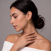 A woman in profile wearing a chunky, polished gold hoop earring, set against a neutral gray background.  The Ever Teardrop Hoop Earrings - The Songbird Collection