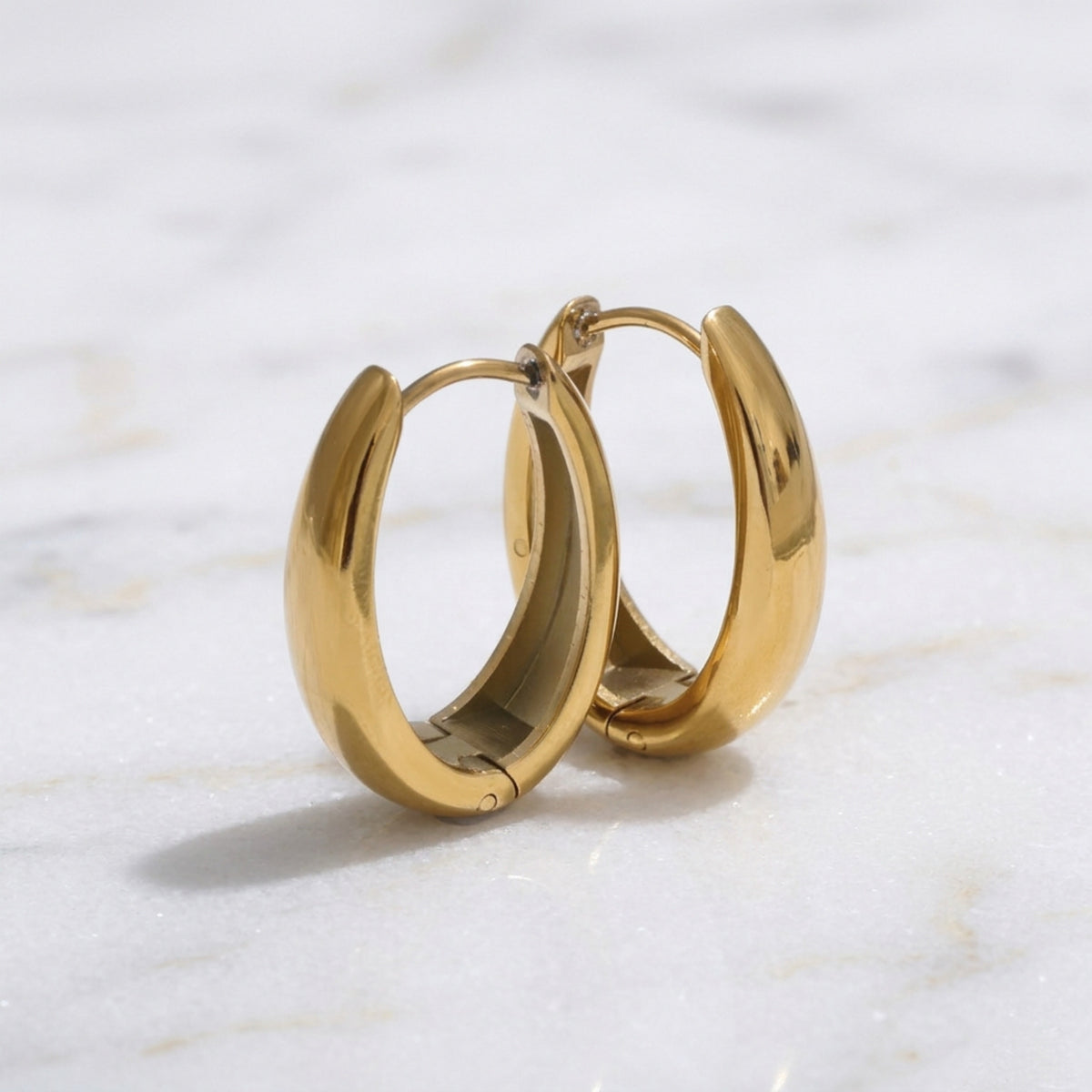 Gold  oblong teardrop hoop earrings on a marble surface