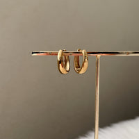 Gold oblong teardrop hoop earrings on a gold stand against a beige background