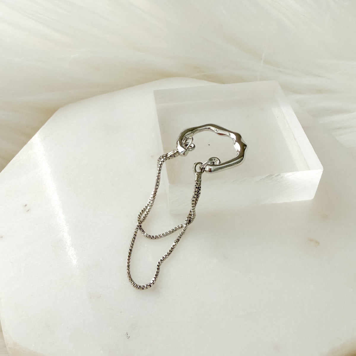 Silver chain ear cuff on a white stone surface