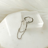 Silver chain ear cuff on a white stone surface