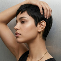Woman with short black hair and gold earrings against a neutral background. The Flow Ear Cuff - The Songbird Collection