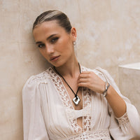 Woman wearing a white lace dress with draped chain earrings, and a black rope pendant necklace against a beige wall