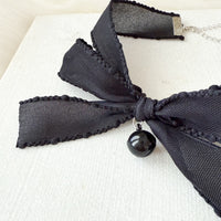 Black bow necklace with a pendant on a light background