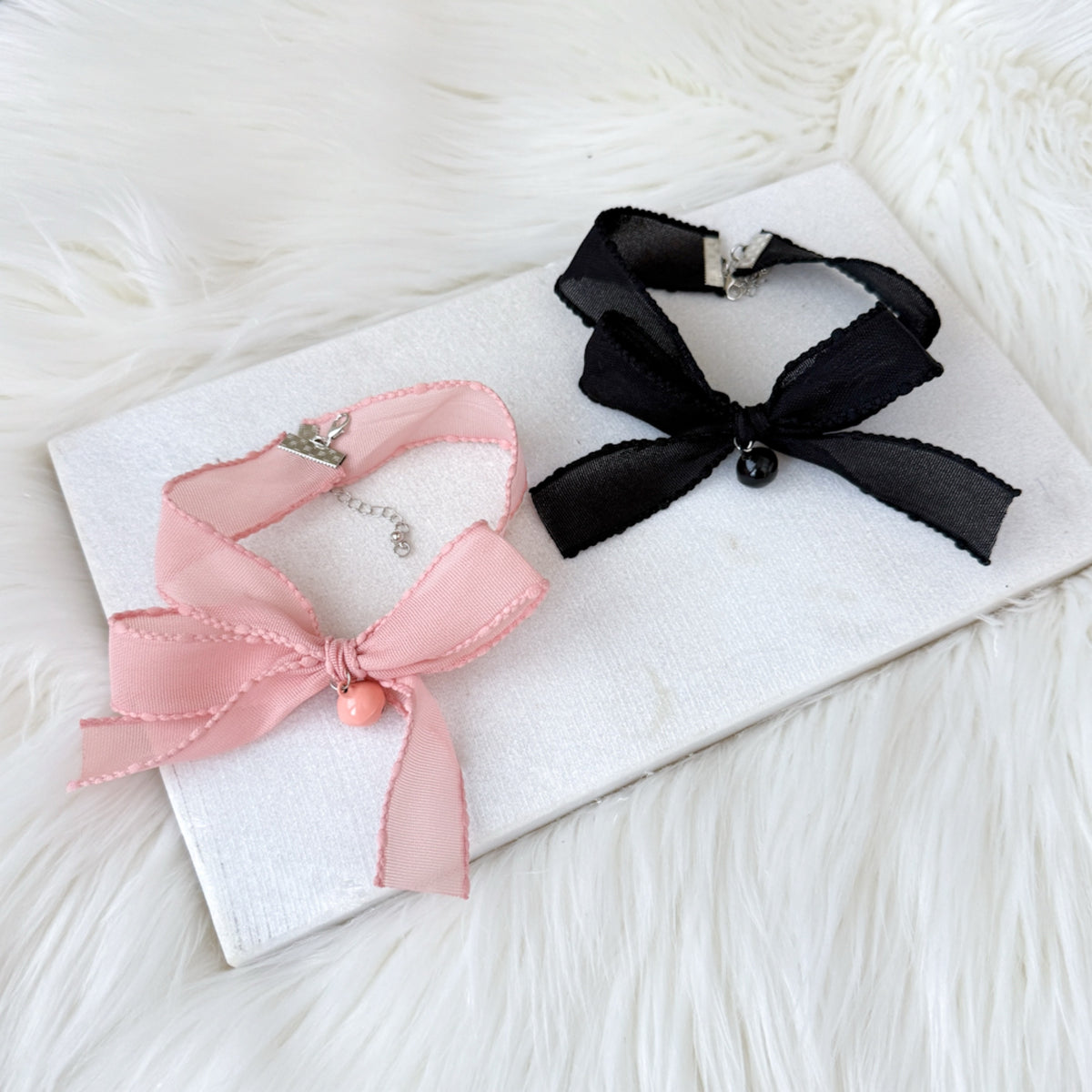 Two ribbon bow tie chokers, one pink and one black, on a white card with a white background.