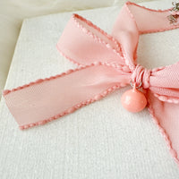 Close-up of a pink bow with a decorative charm on a white background