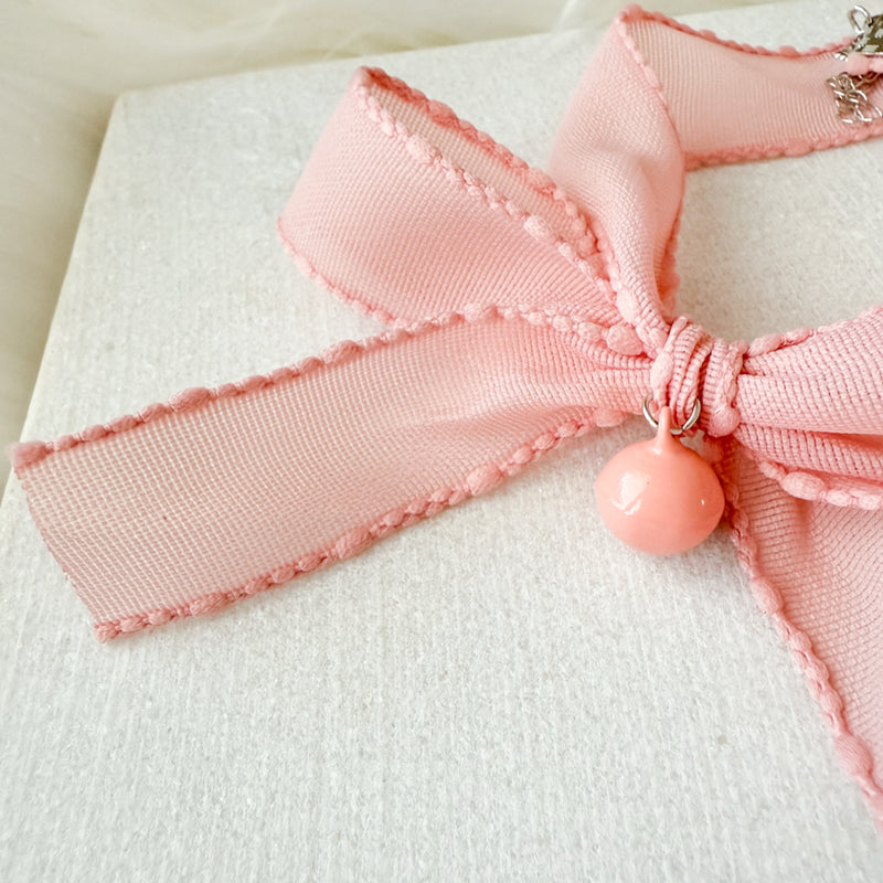 Close-up of a pink bow with a decorative charm on a white background