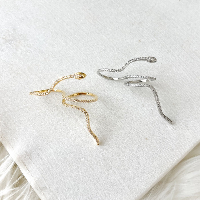 Two twisted serpent double finger rings, one plated in gold and the other in silver, placed on a white fabric surface.