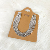 A rhinestone necklace displayed on a beige card against a white fluffy background.