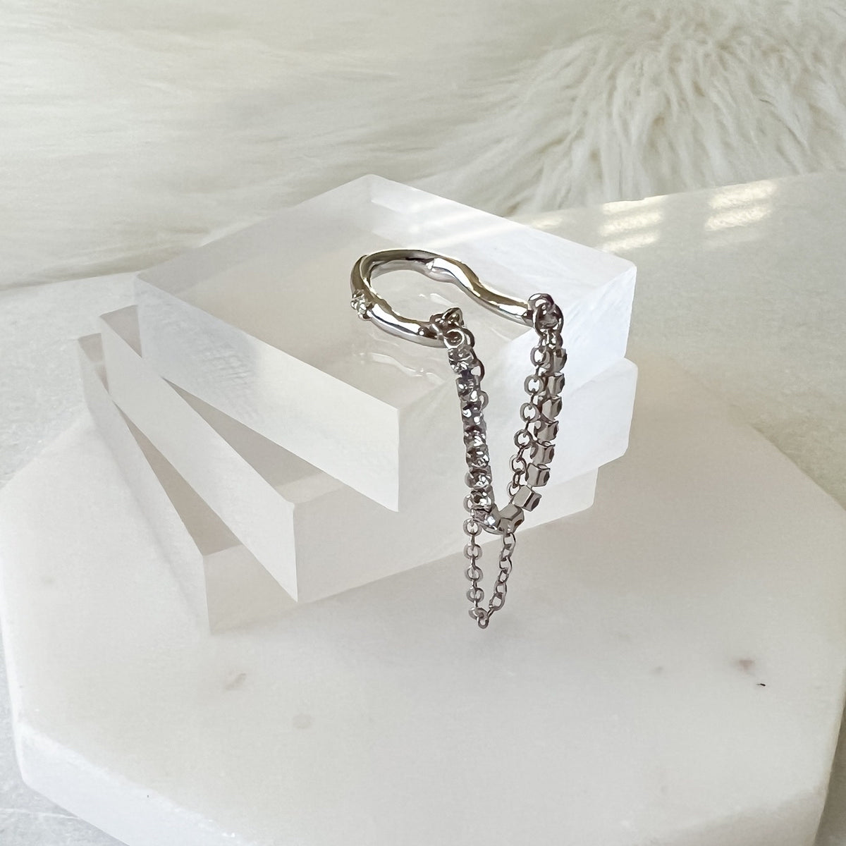 A silver ear cuff featuring two strands of dropping chains displayed on a white surface.