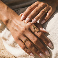 Close-up of hands with gold rings and light pink nail polish on a textured beige background  gothic_throne_ring - Tessa Ring Set- The Songbird Collection