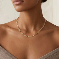 Close-up of a person wearing a gold  wavy necklace against a neutral background - stainless steel silver wavy chain necklace a marble surface - Aura_Ripple_Chain_Necklace_-_The_Songbird_Collection